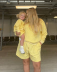 Woman in a yellow outfit holding a child in an airport terminal.