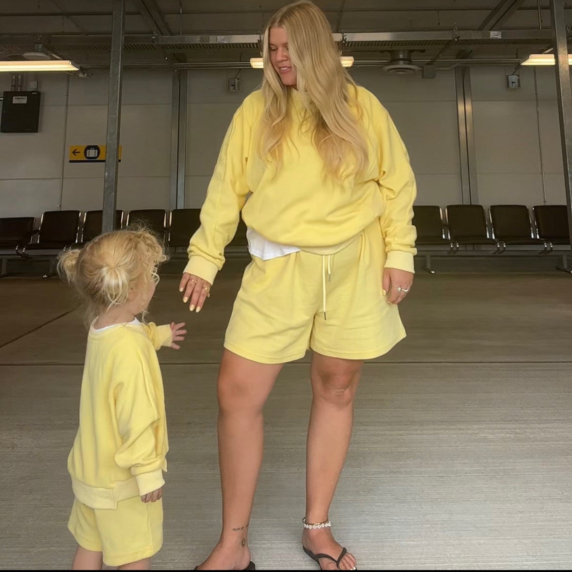 Two people in matching yellow outfits standing in a large indoor space with high ceilings.