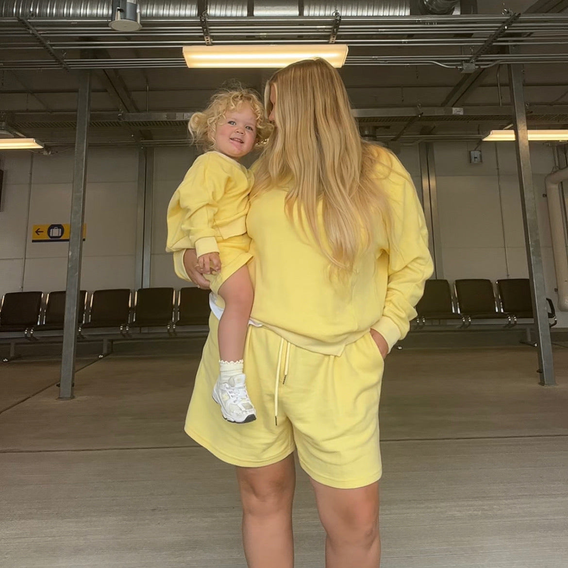 Woman in a yellow outfit holding a child in an airport terminal.